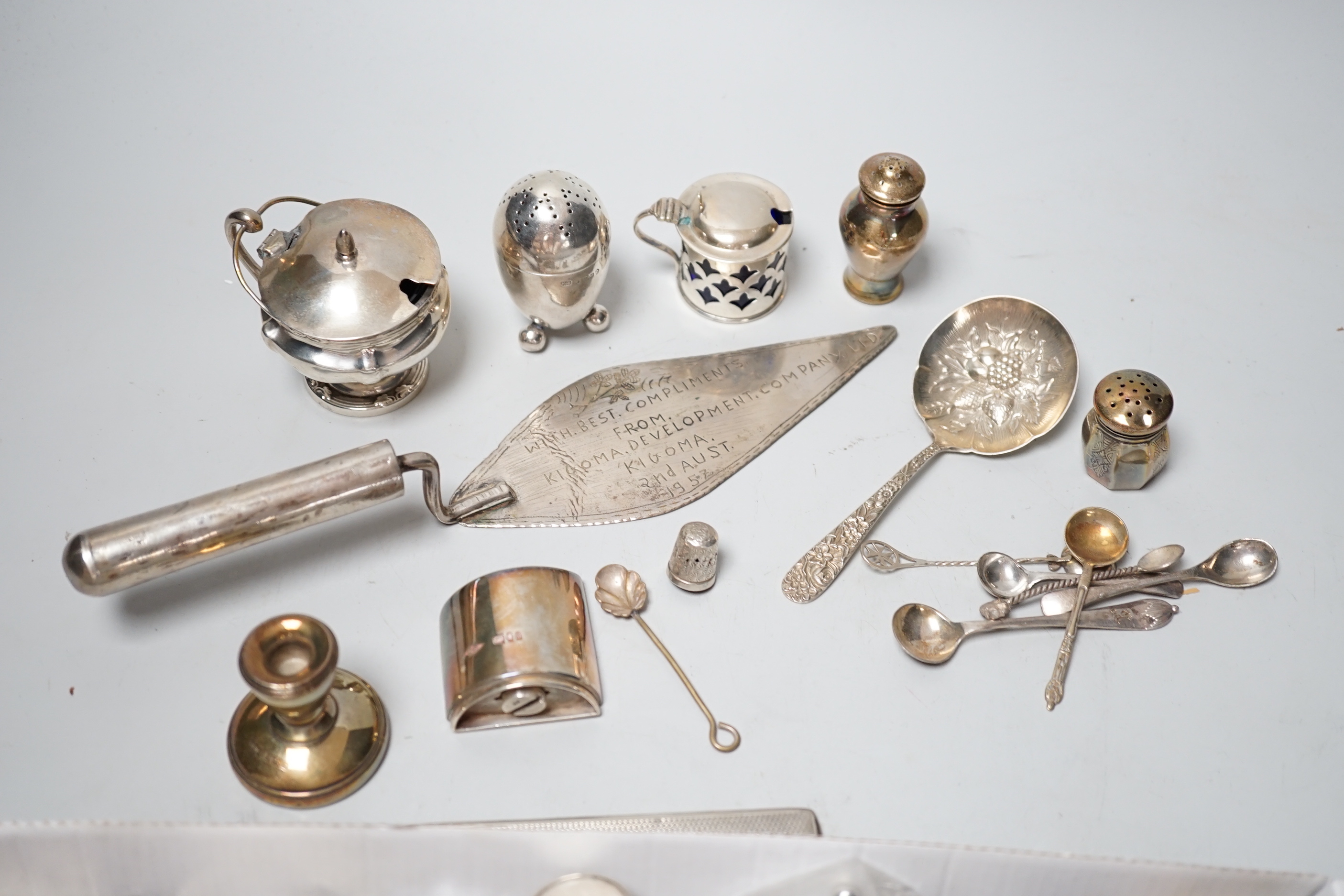 A collection of assorted small silver including condiments, spoons, egg cup, pill box, comb, Tiffany & Co pen, dwarf candlesticks, and other items including a plated evening bag and African trowel.